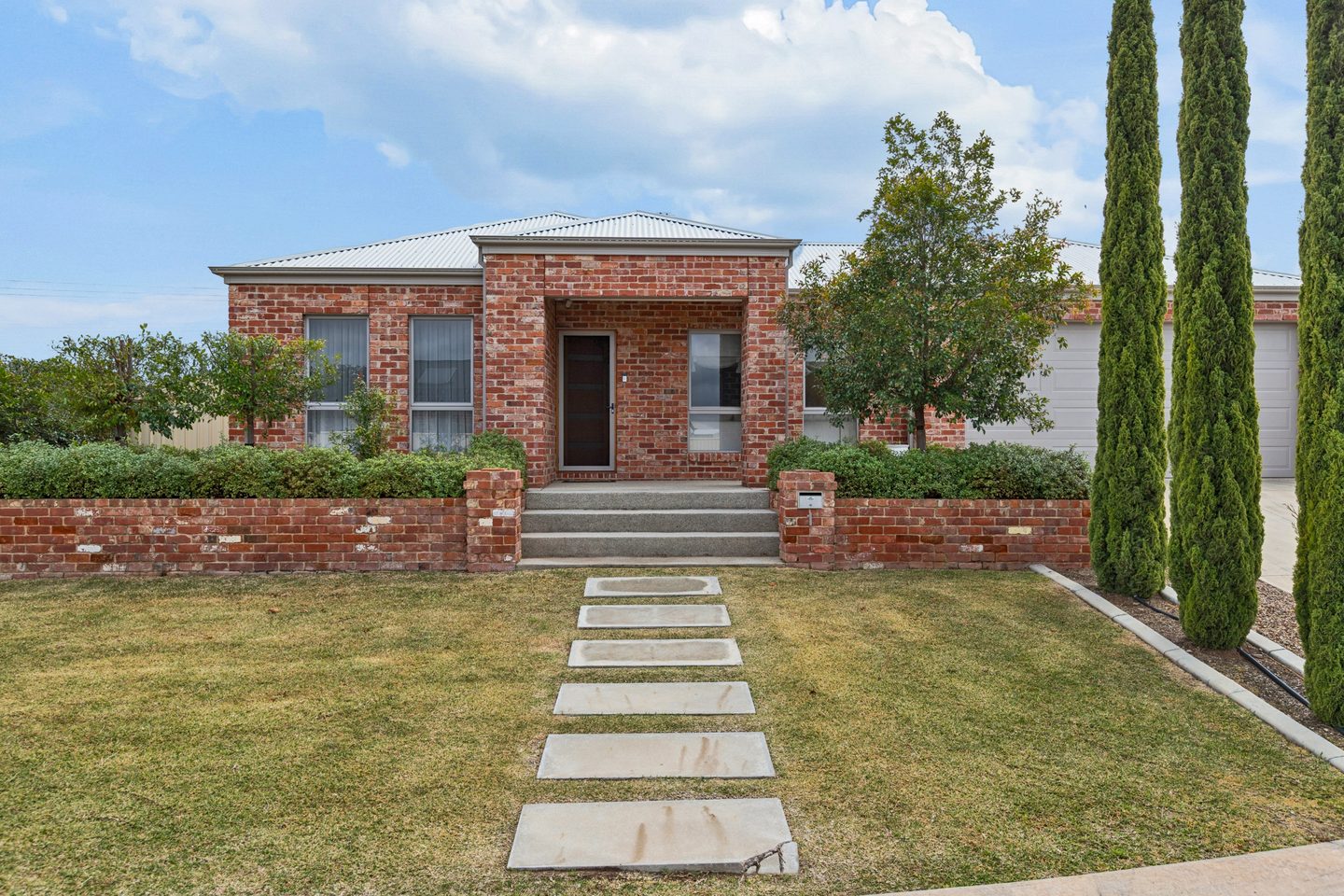 Red-brick frontage with a stepping-stone path, lawn and tall slender trees