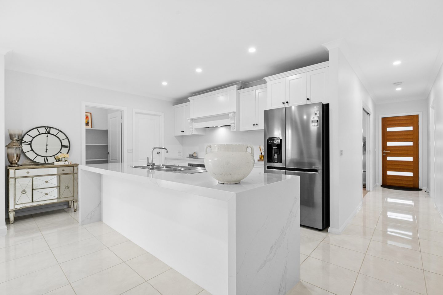White kitchen with a broad island, panelled cabinetry and adjacent pantry