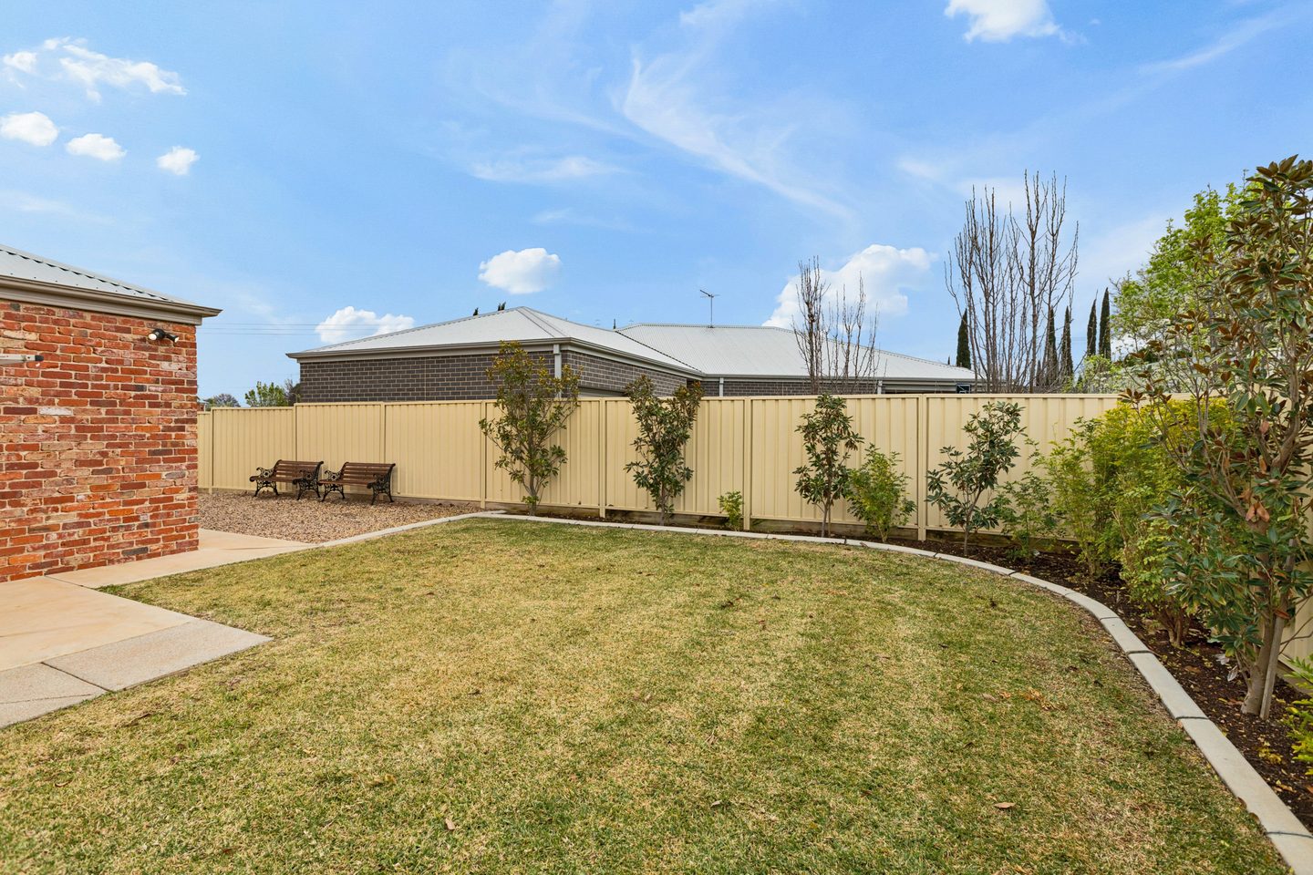 Rear lawn edged by garden beds, with a gravel side area