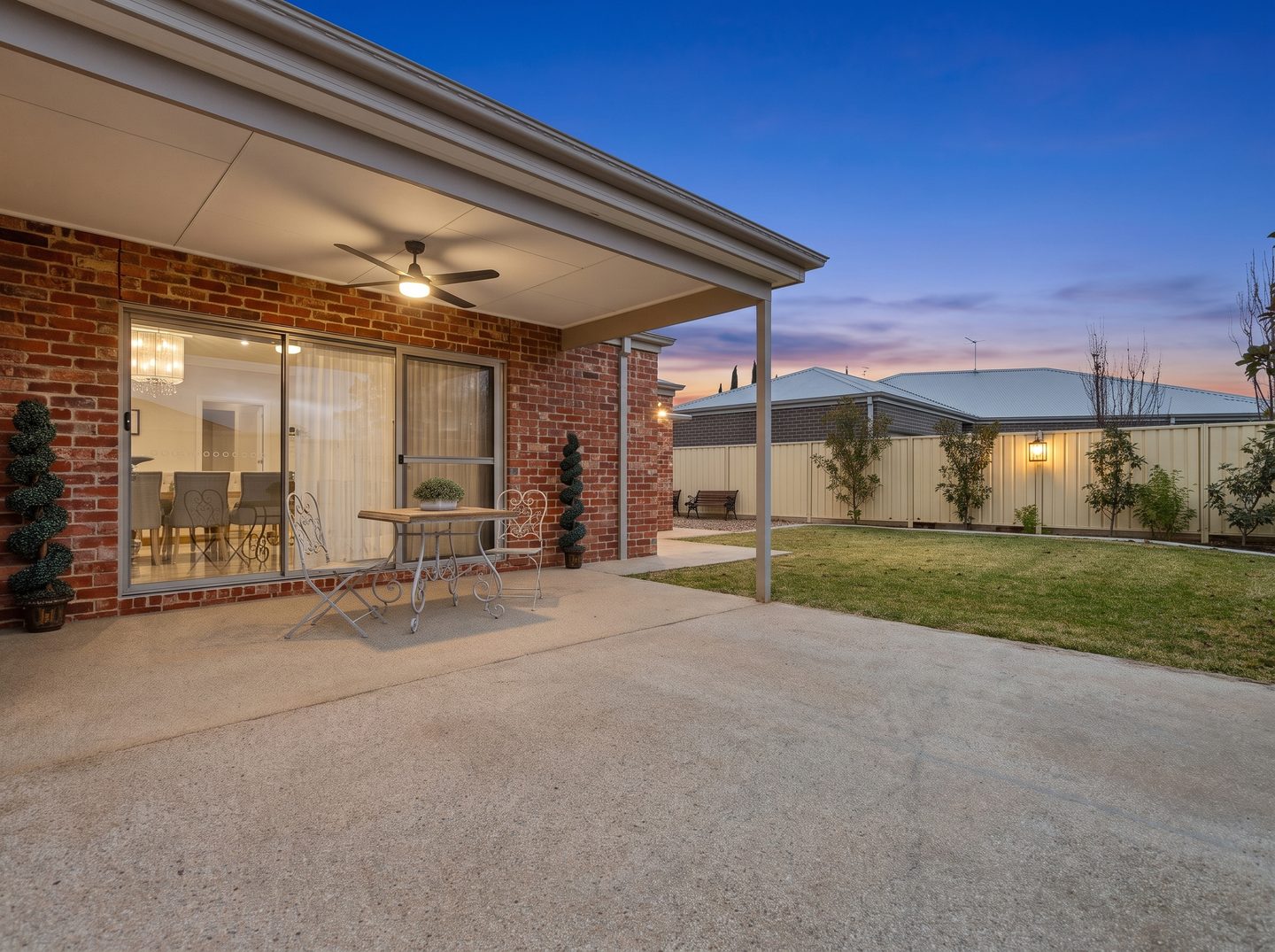 Covered brick patio with ceiling fan and adjoining lawn in the evening